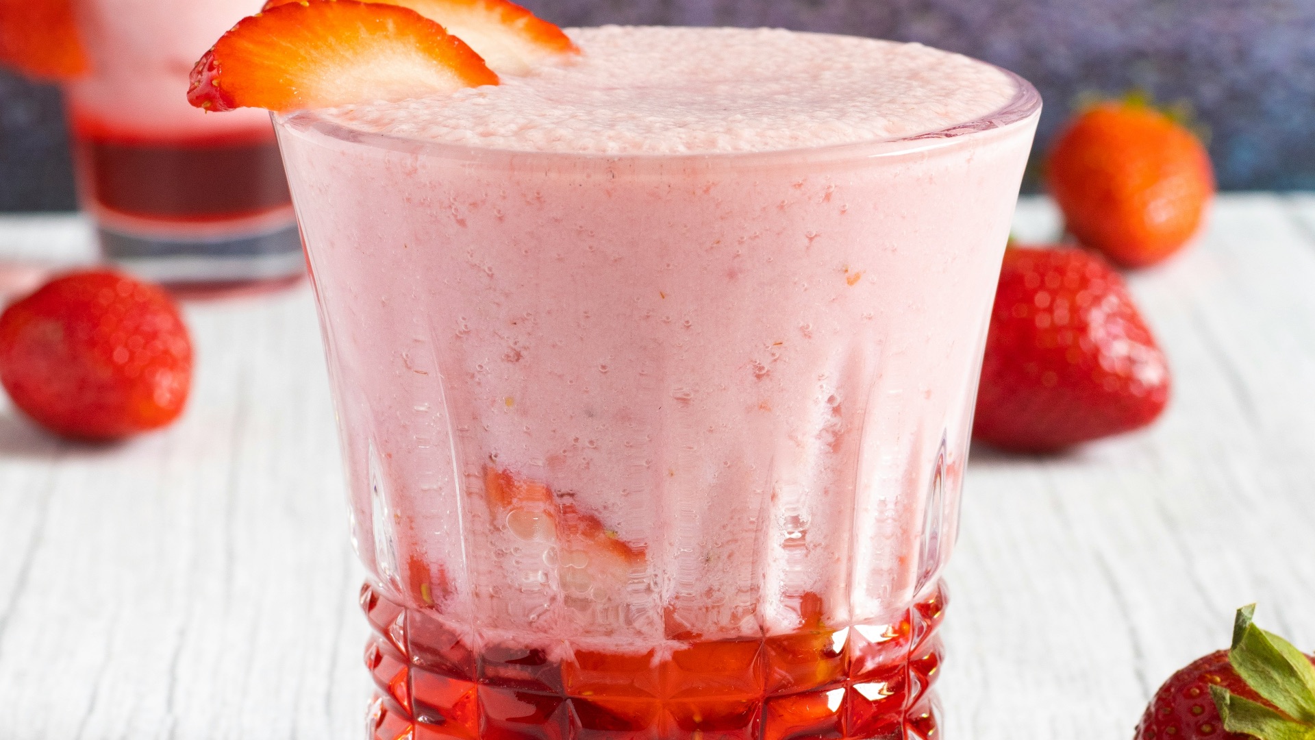 two glasses of strawberry milkshake with strawberries on the side