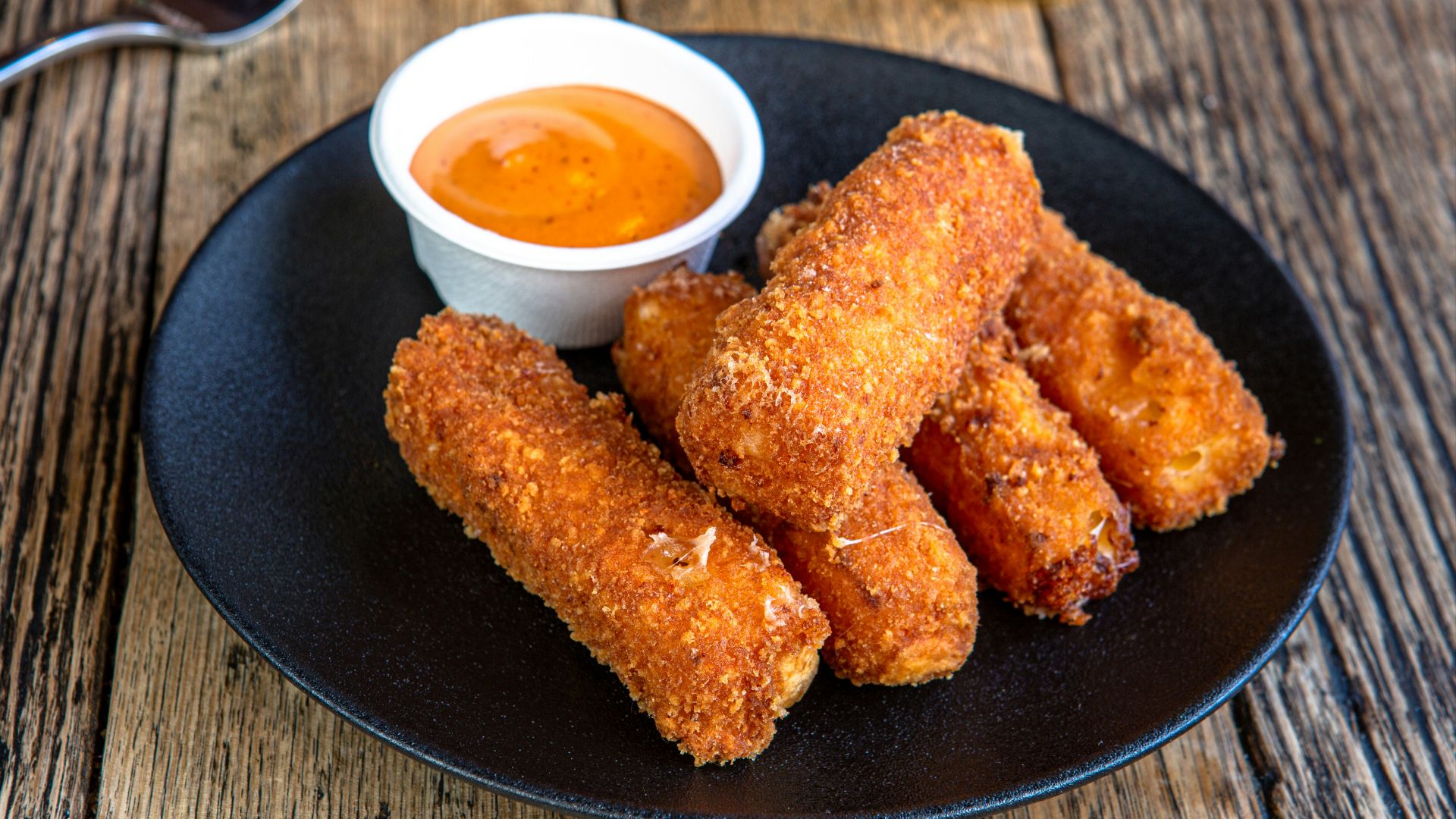 A black plate topped with fried food next to a cup of dipping sauce