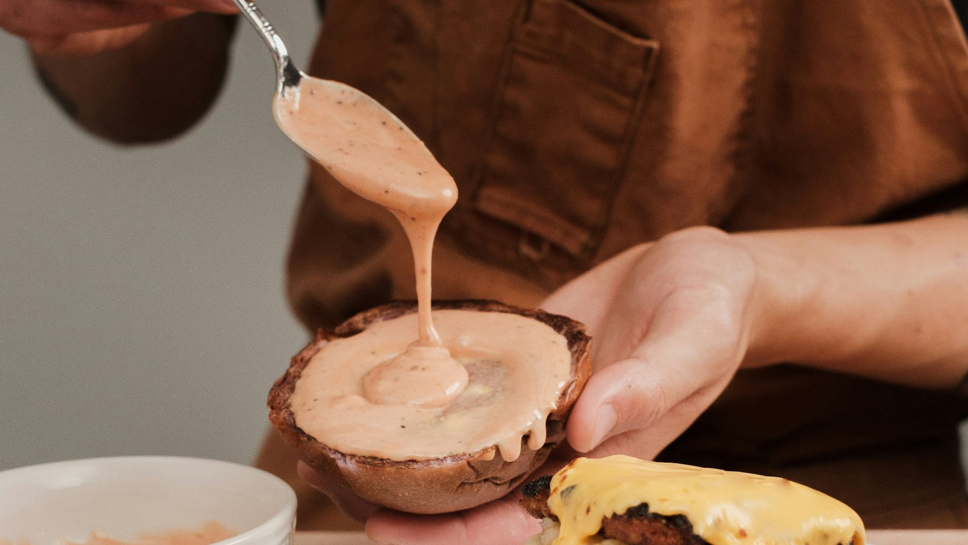 a person is spreading sauce on a hamburger