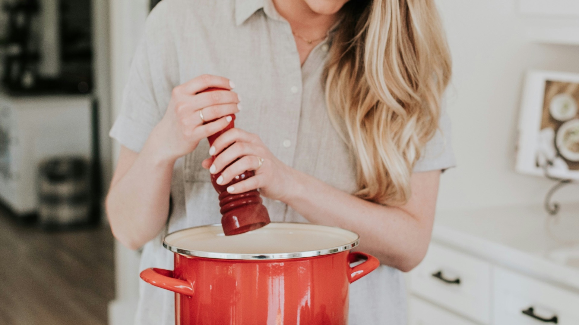 smiling woman standing and putting pepper on stock pot