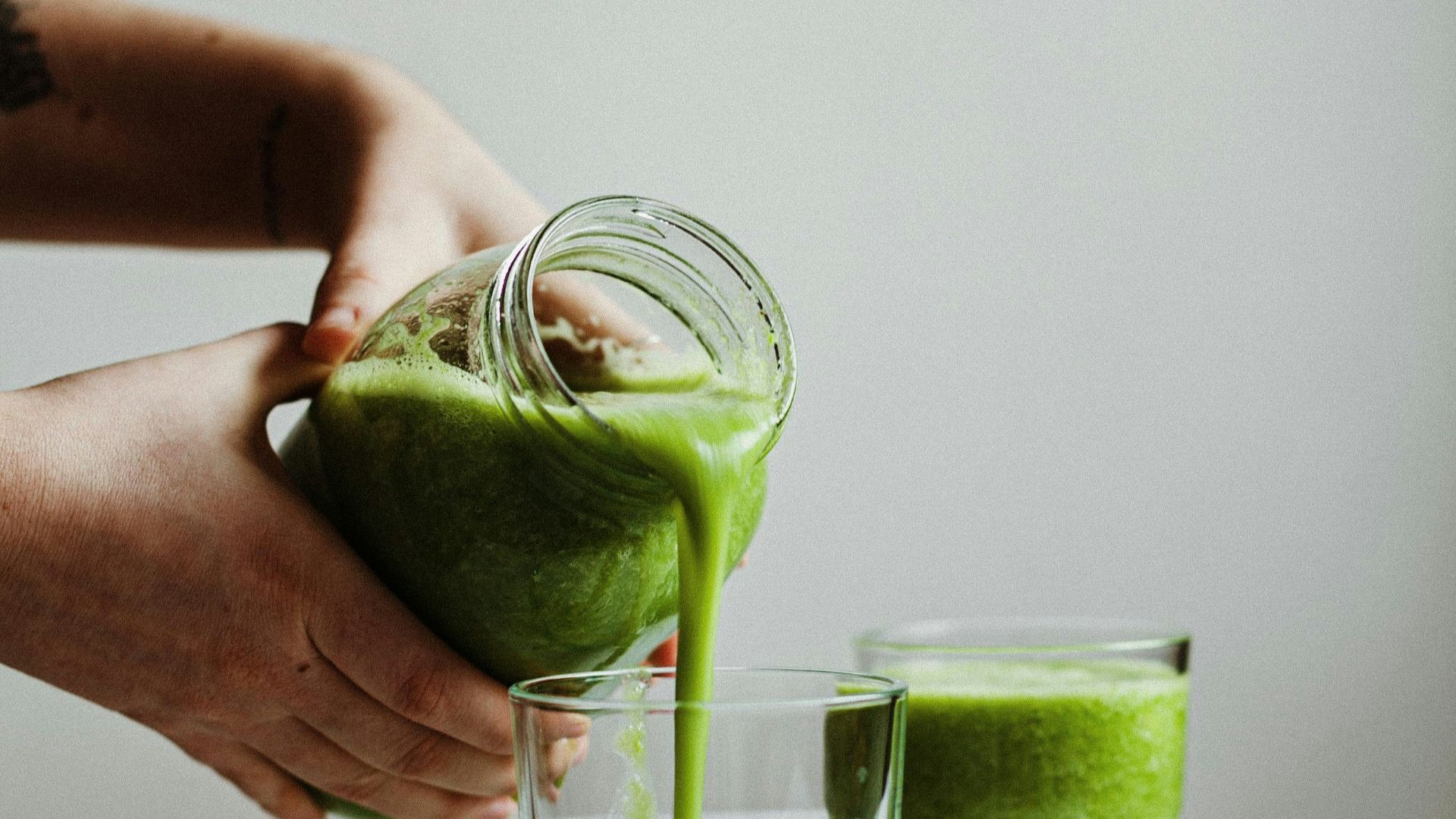 person holding clear drinking glass with green liquid