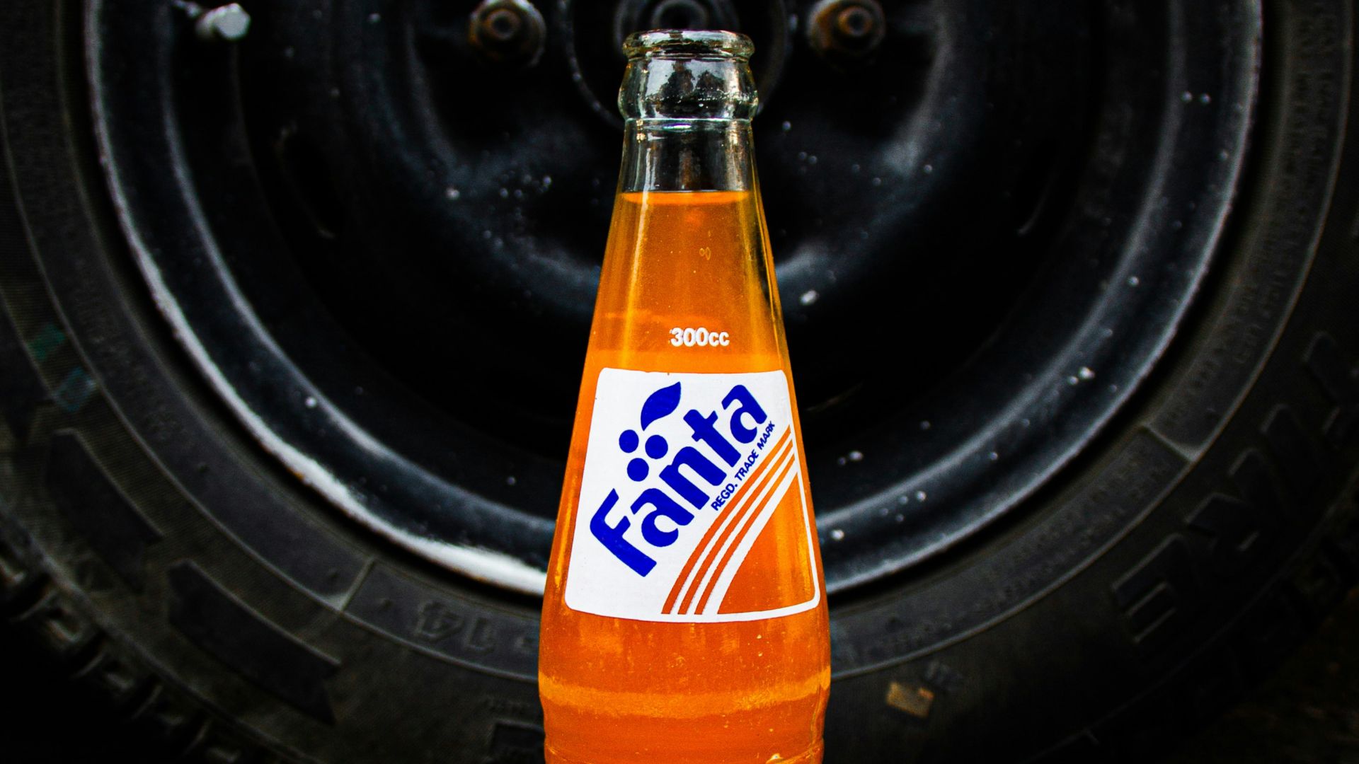 a bottle of soda sitting on the ground next to a tire