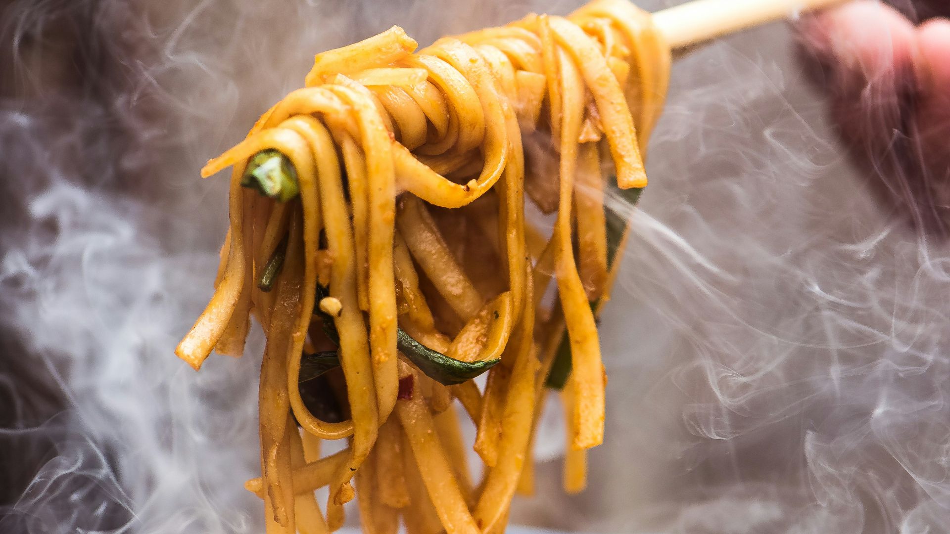 a person holding a wooden spoon full of noodles