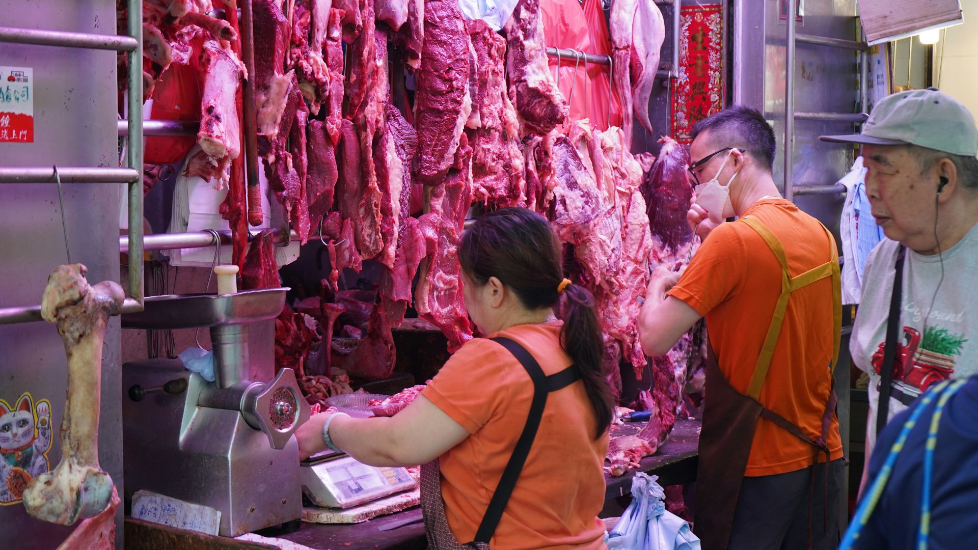 Butchers working at a meat stall with hanging carcasses.