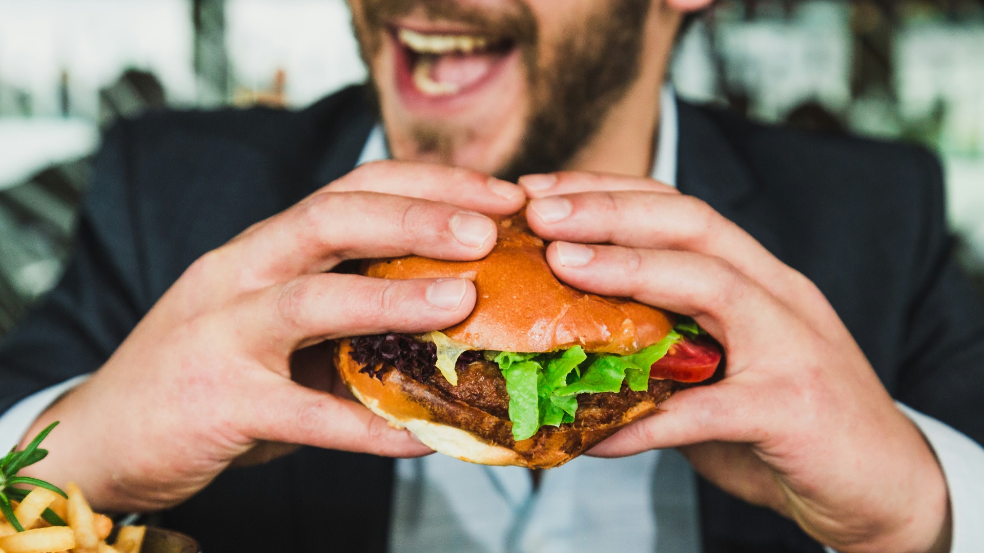 person holding burger bun with vegetables and meat
