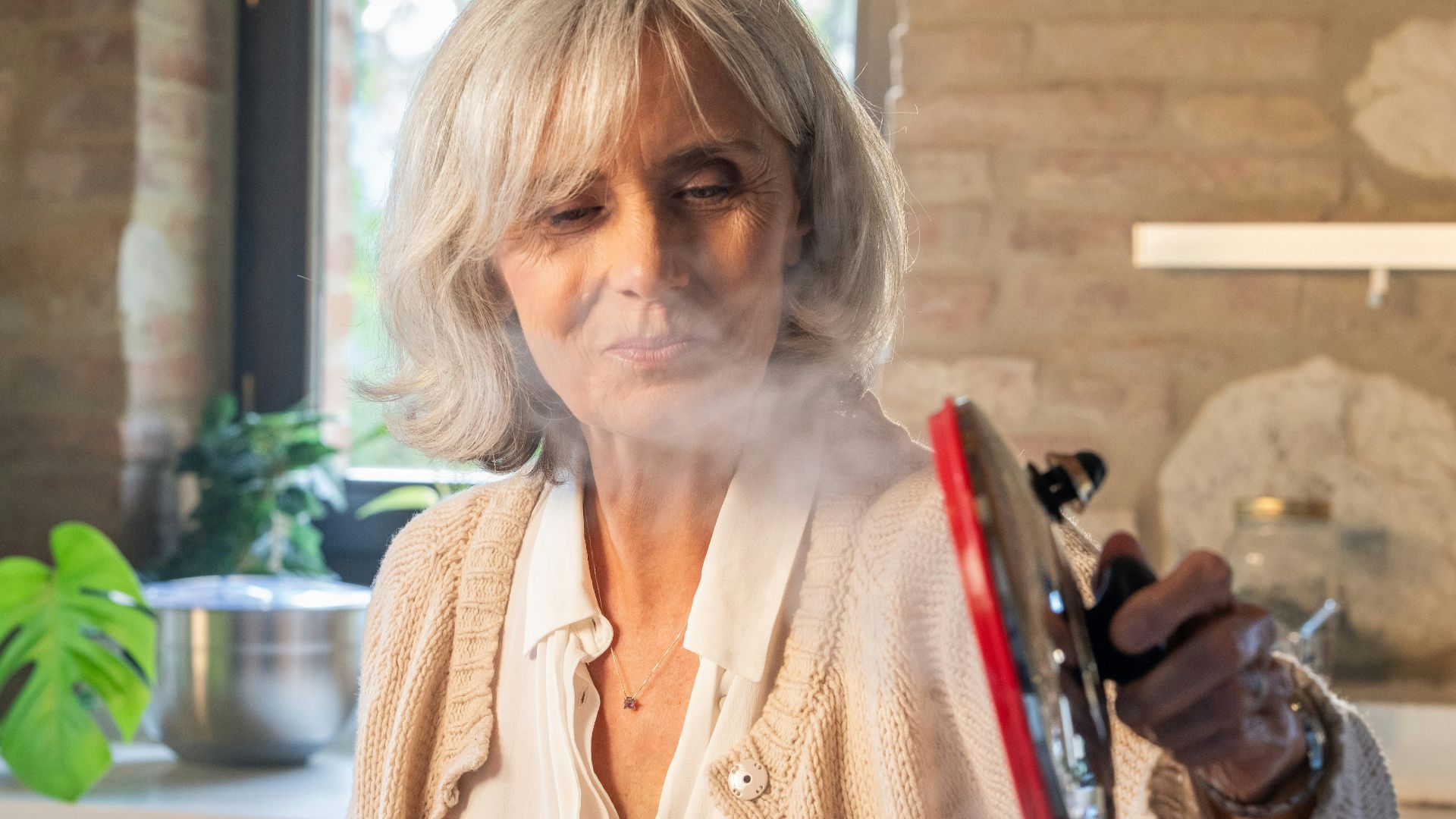 Elderly woman lifting lid from steaming pot