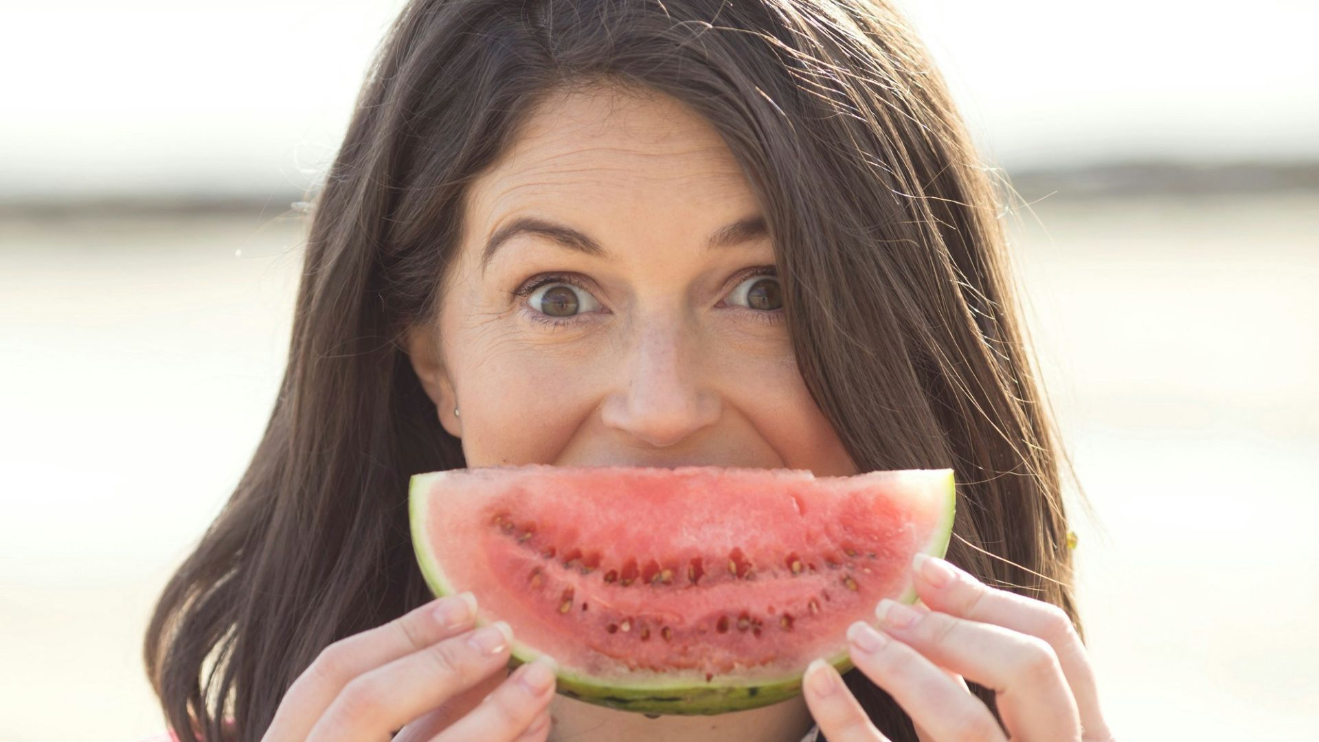 a woman holding a slice of watermelon up to her mouth