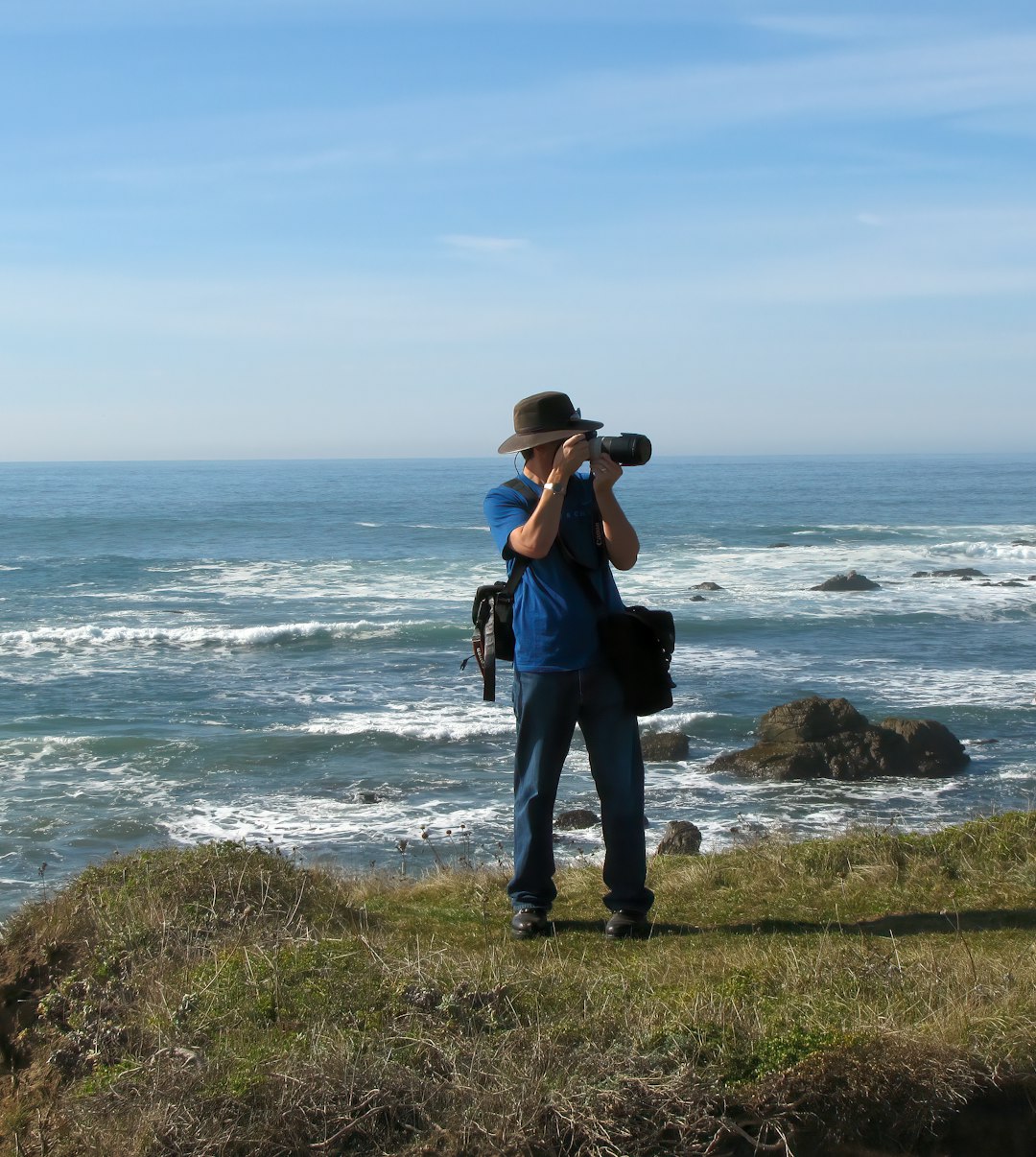 a man standing on top of a lush green hillside next to the ocean