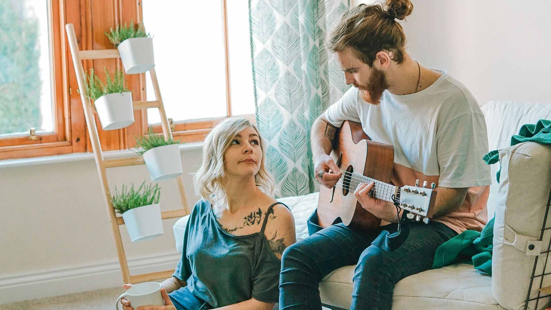 man sitting on sofa playing guitar looking at girl sitting on the ground near window inside room