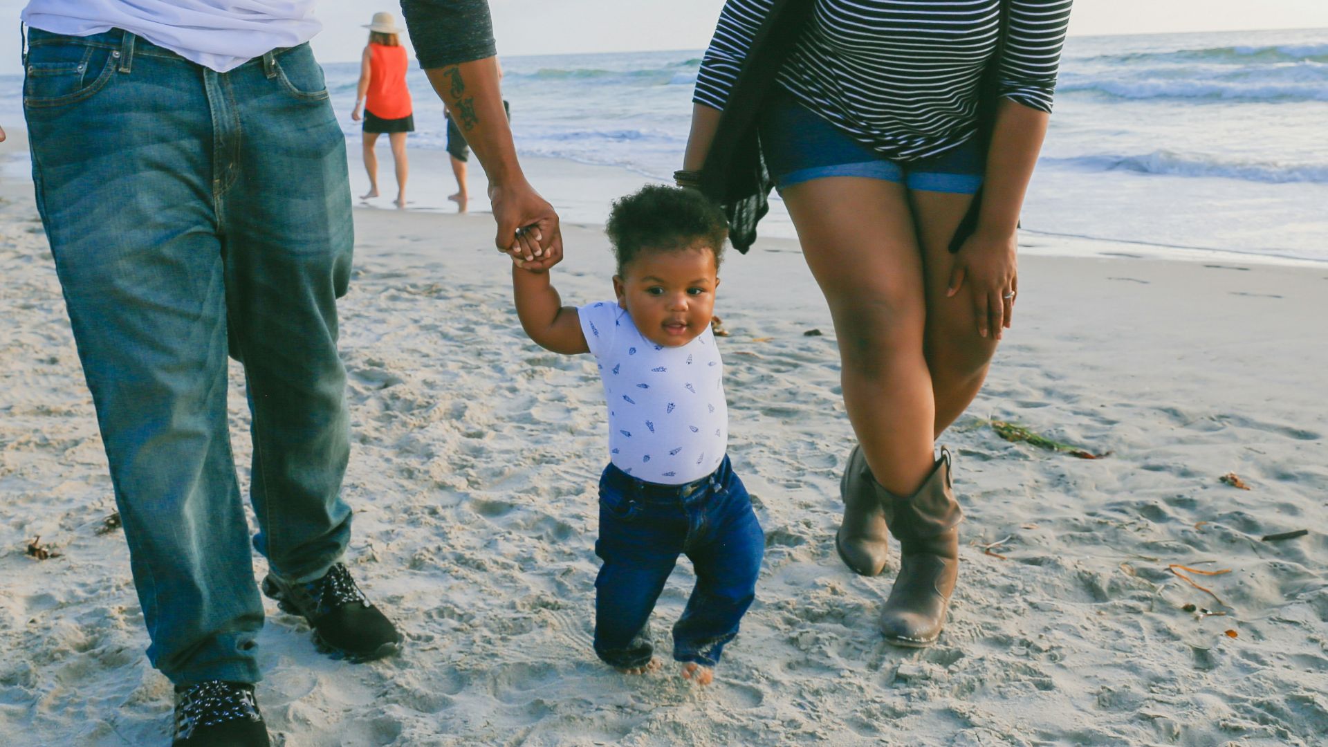 man in black and white striped long sleeve shirt holding baby in white shirt on beach