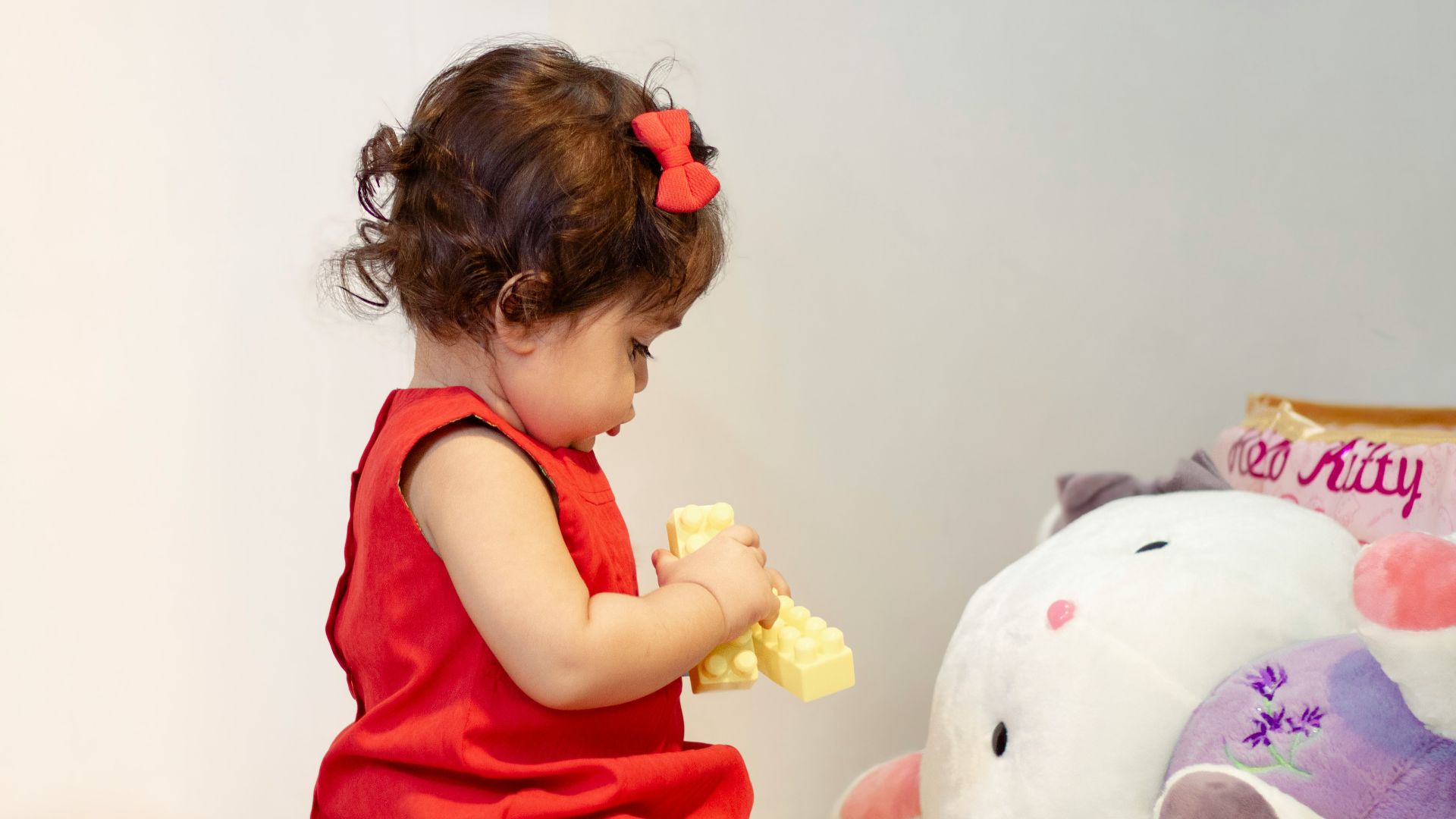 a little girl in a red dress playing with a stuffed animal