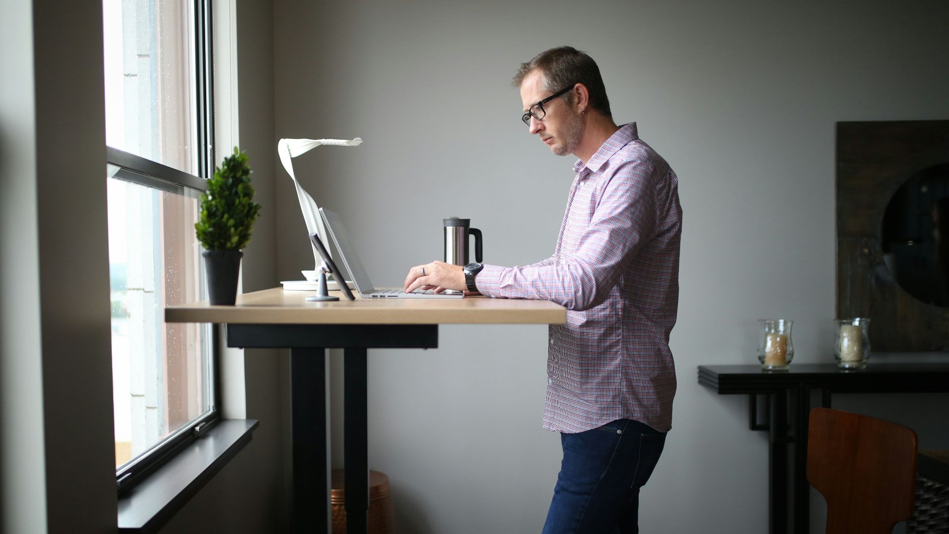 man in pink dress shirt and blue denim jeans standing beside brown wooden table