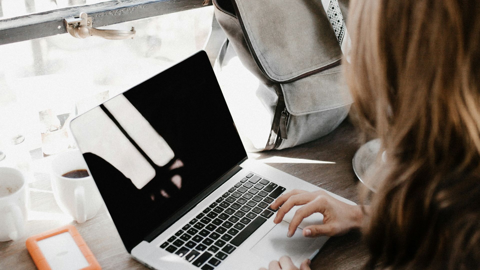 girl wearing grey long-sleeved shirt using MacBook Pro on brown wooden table