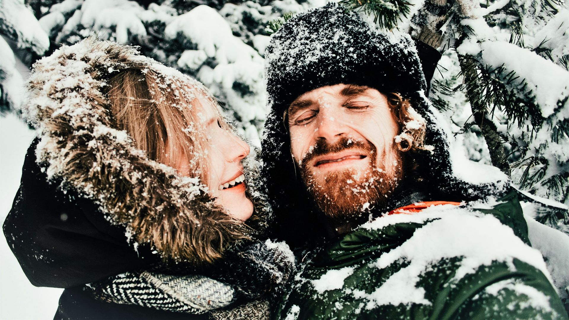 smiling man and woman standing under snow covered tree