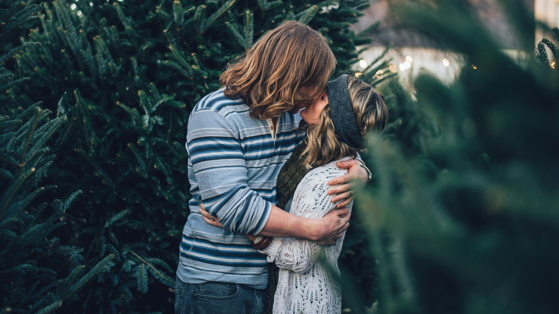 man kissing woman near pine tree