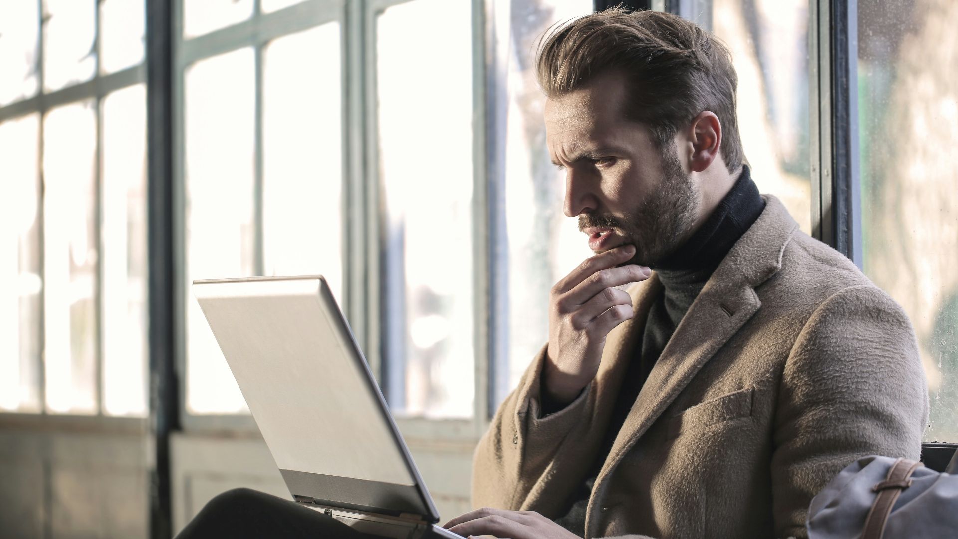 man holding his chin facing laptop computer