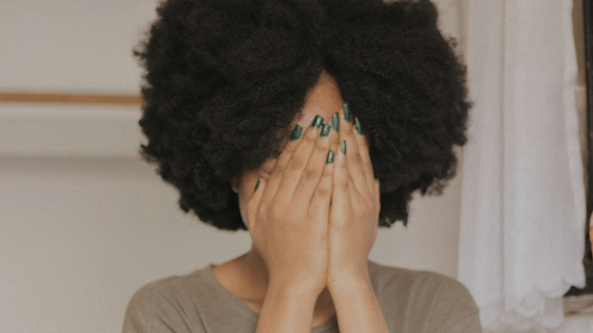 woman in gray t-shirt covering face with both hands