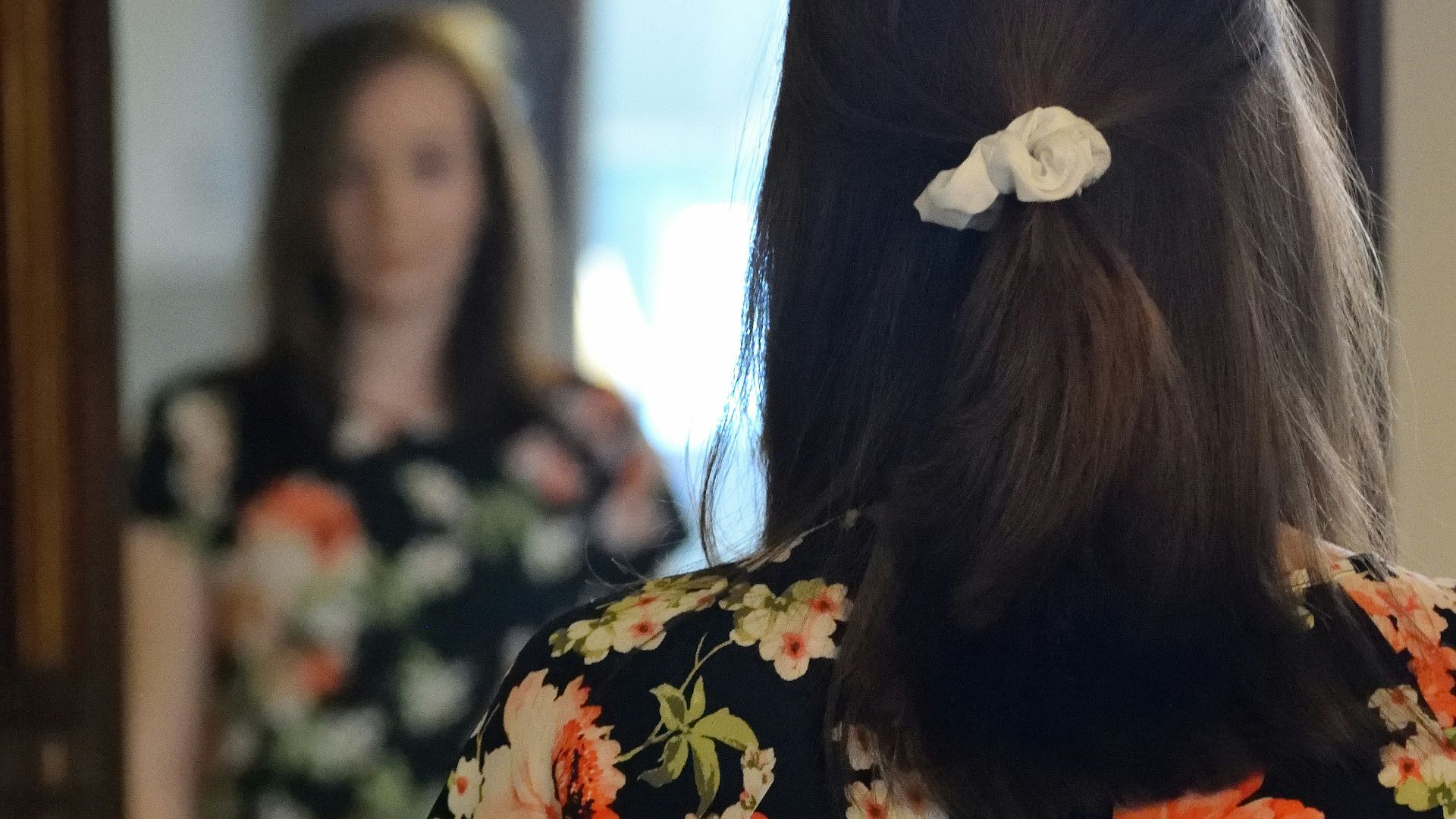 woman wearing black and multicolored blouse and blue denim jeans facing mirror inside white concrete room