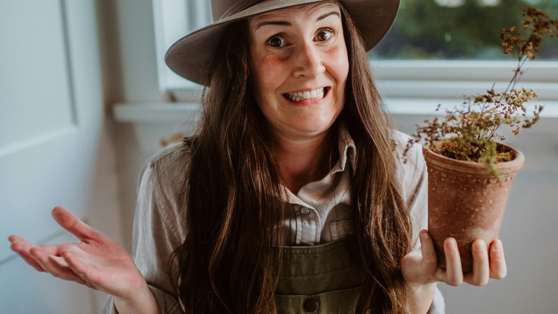 A woman wearing overalls and a hat holding a potted plant