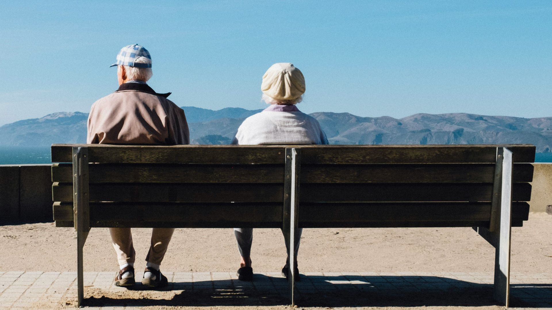 man and woman sitting on bench facing sea