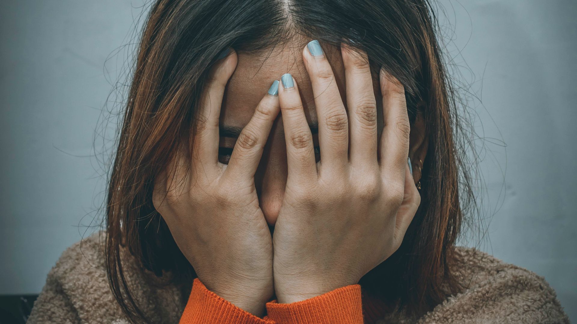 woman in brown sweater covering her face with her hand
