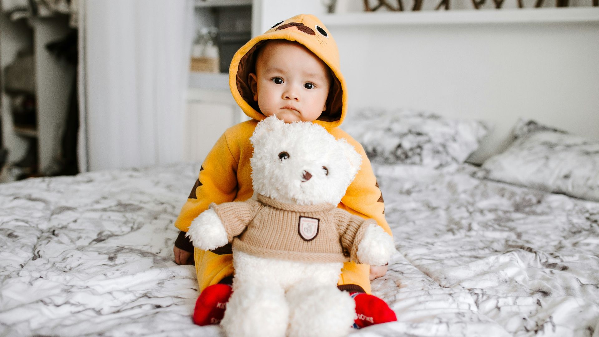 toddler sitting on bed beside white bear plush toy