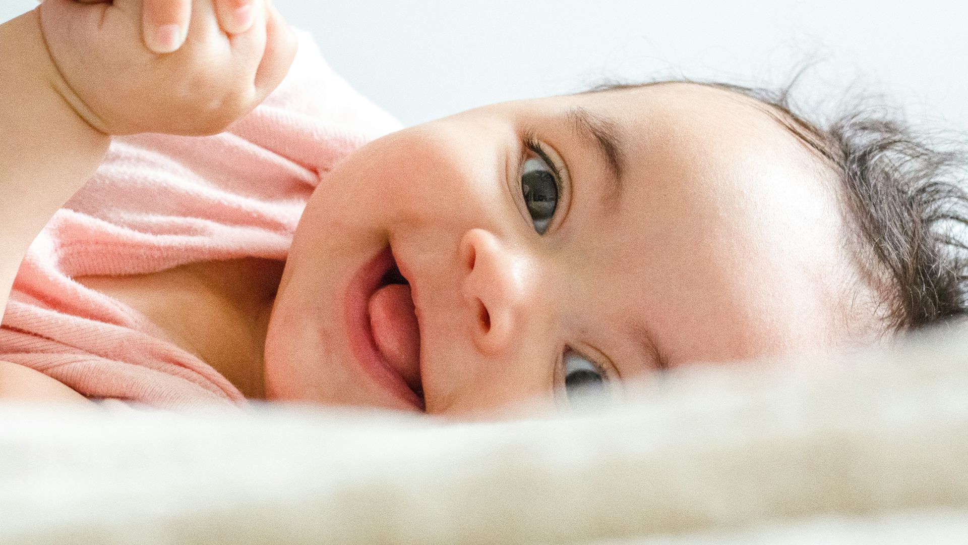 baby in pink shirt lying on white textile