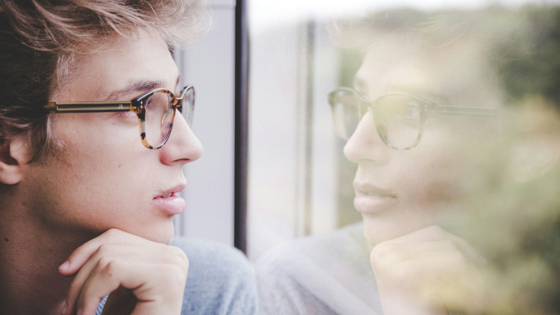 a man wearing glasses looking out a window