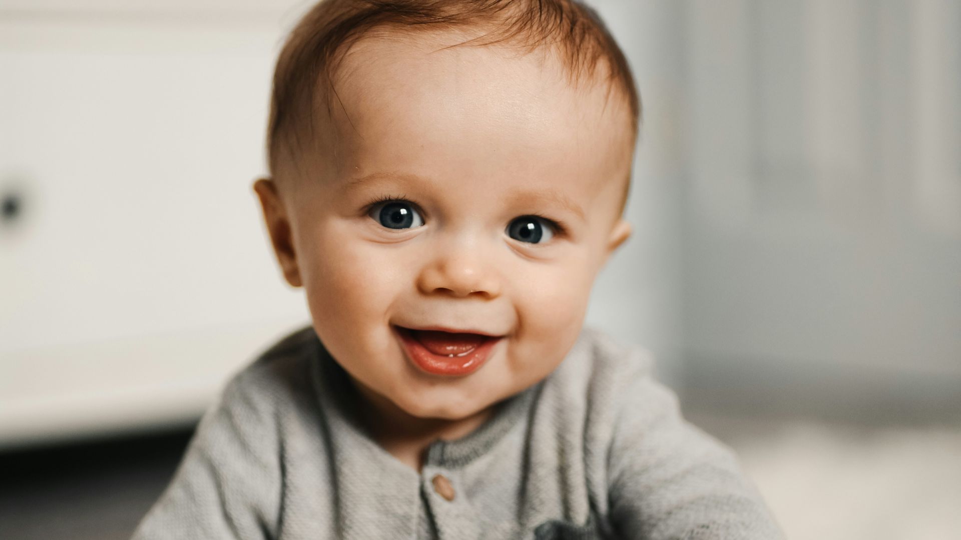 baby in gray sweater lying on white textile