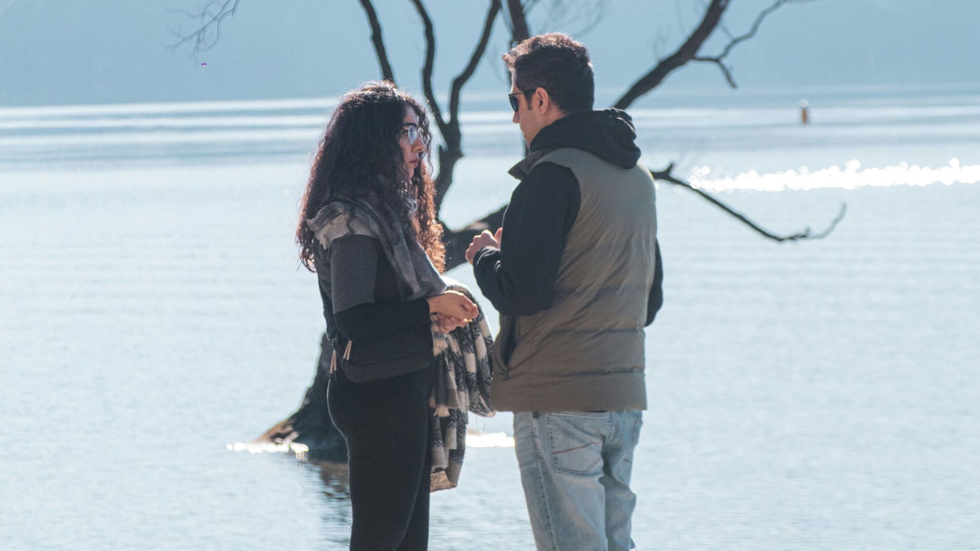 A man and woman standing on a beach next to a tree