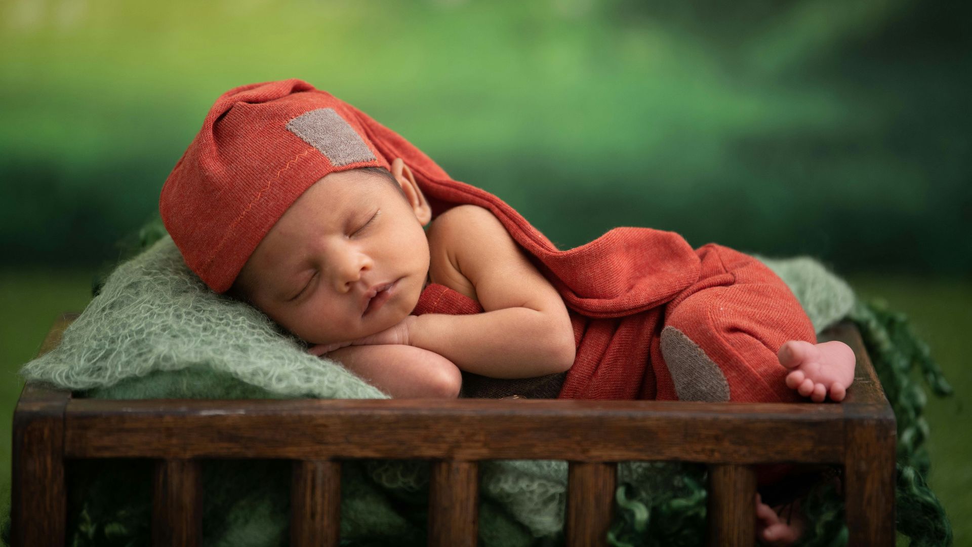 baby in red blanket lying on green textile
