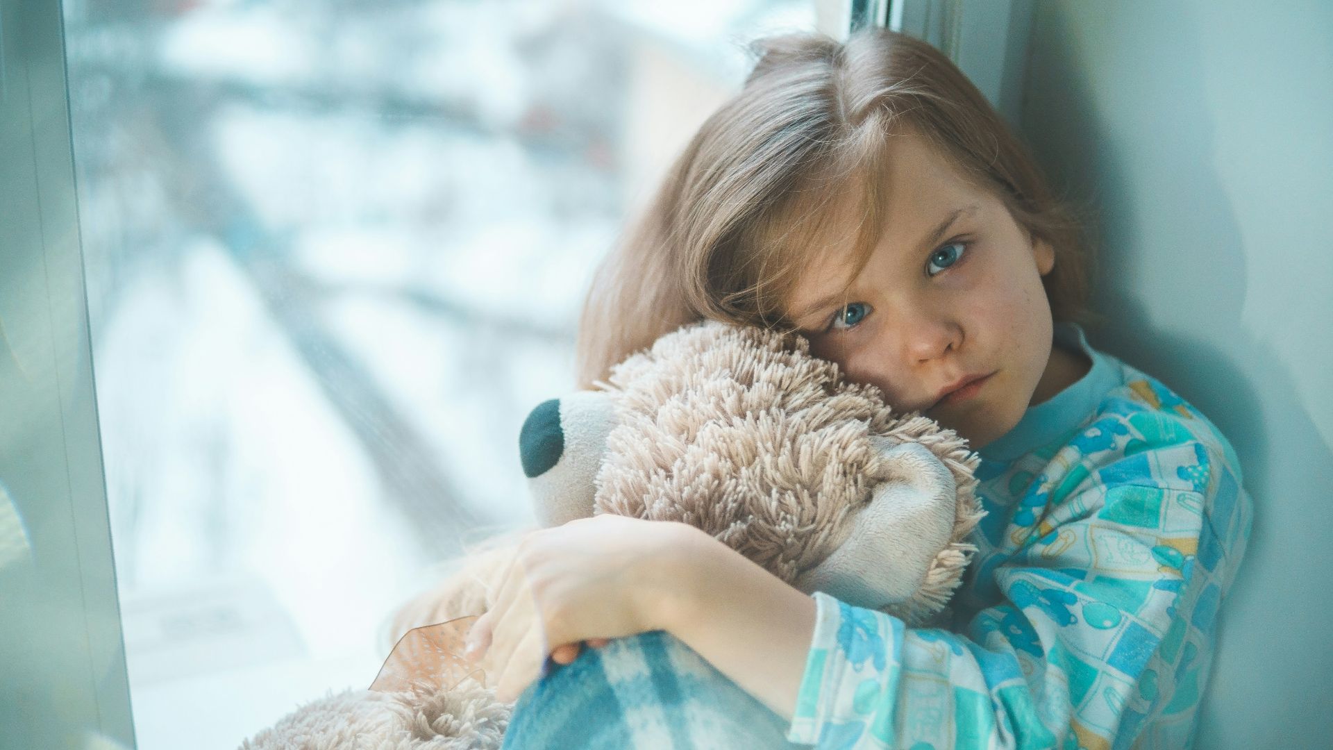 girl in blue white and red plaid shirt hugging brown teddy bear