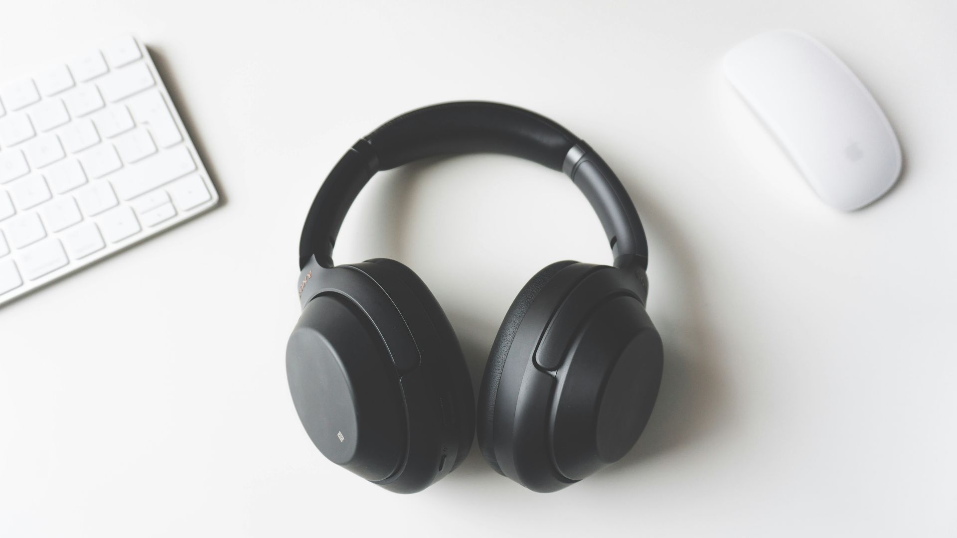black wireless headphones between Apple Keyboard and Apple Magic Mouse on white surface
