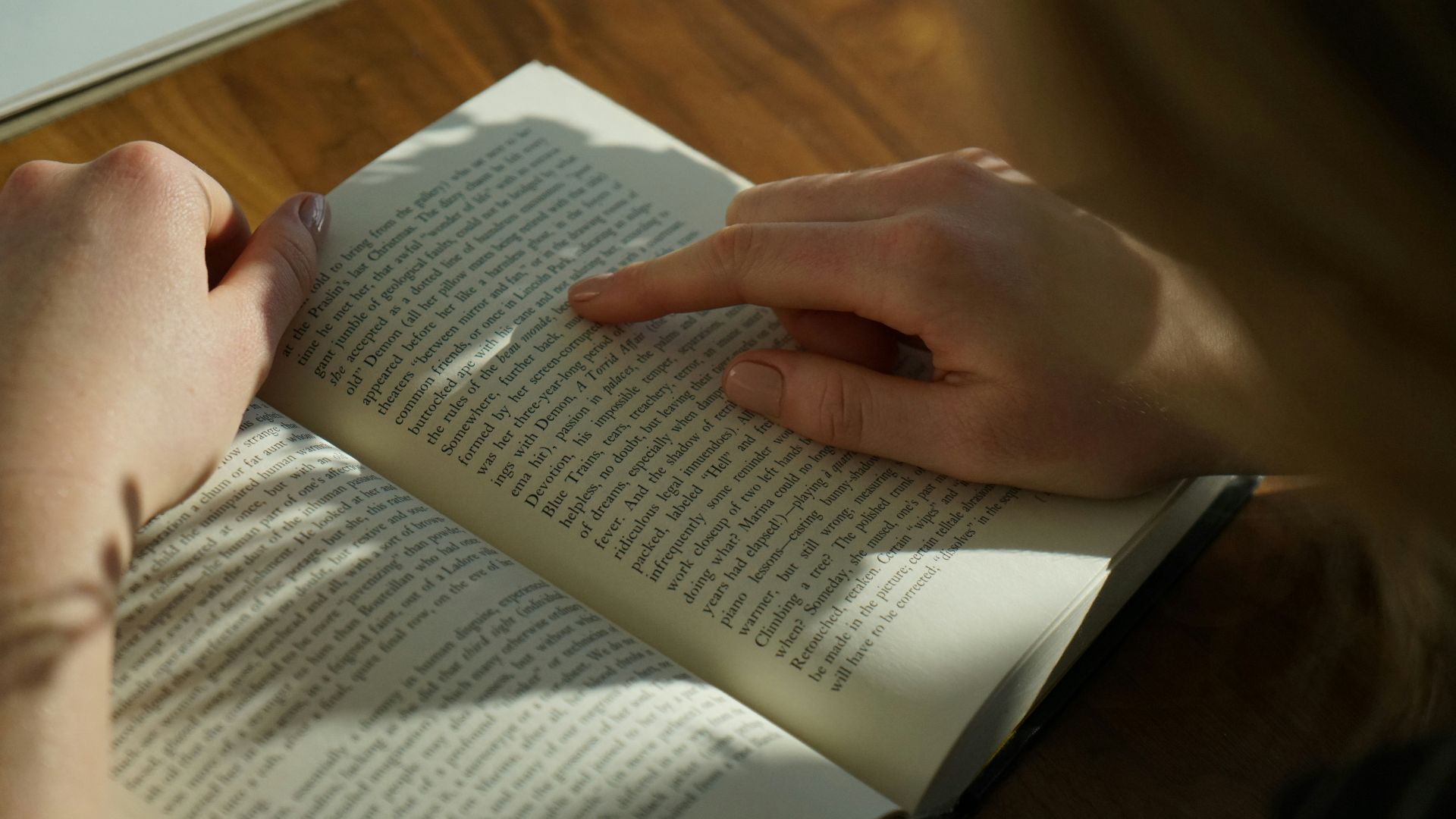 person reading book on brown wooden table taken at daytome