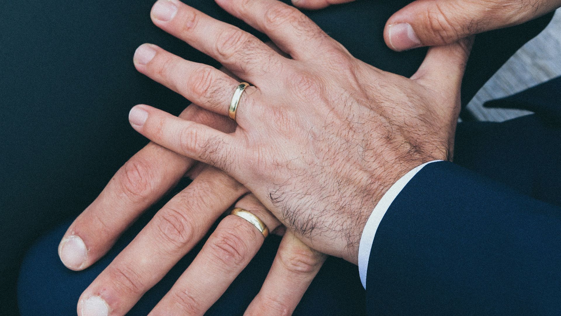 two man's hands wearing gold-colored wedding rings