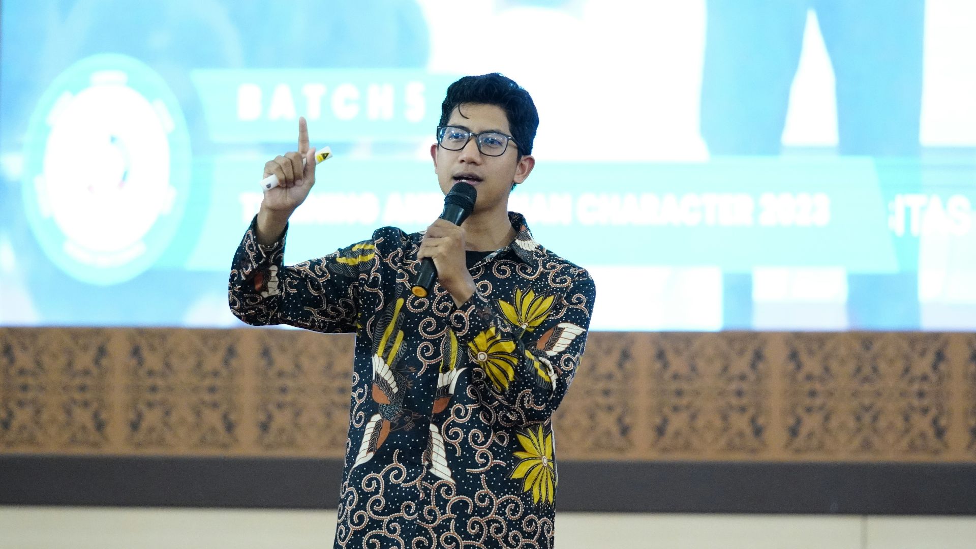 a man standing in front of a screen holding a microphone