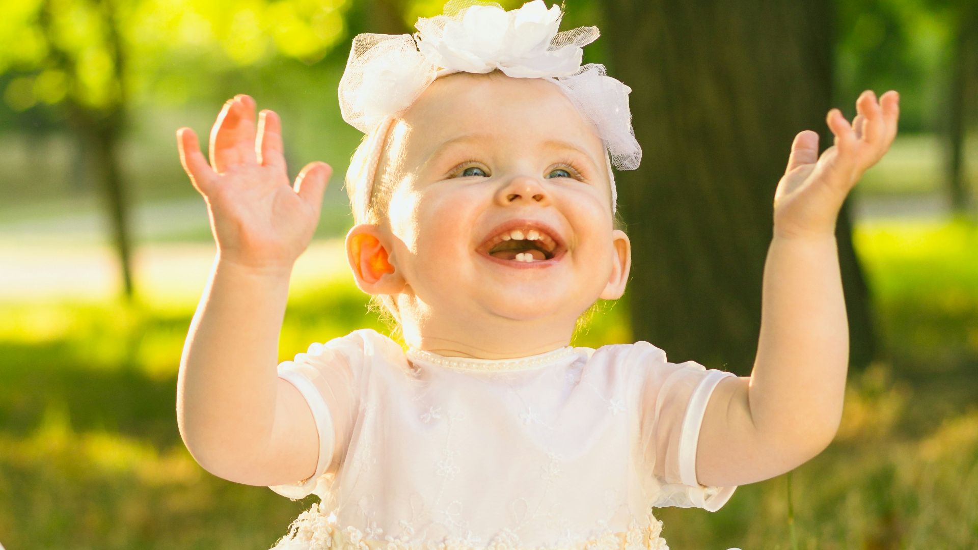 a baby girl in a white dress sitting in the grass