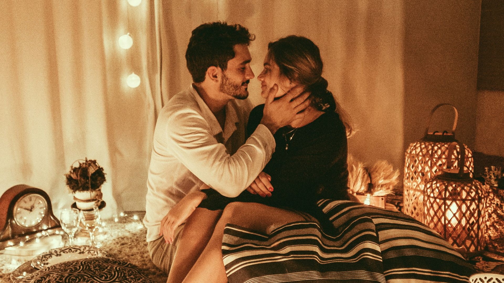 man and woman sitting on floor and about to kiss with lighted candles inside room
