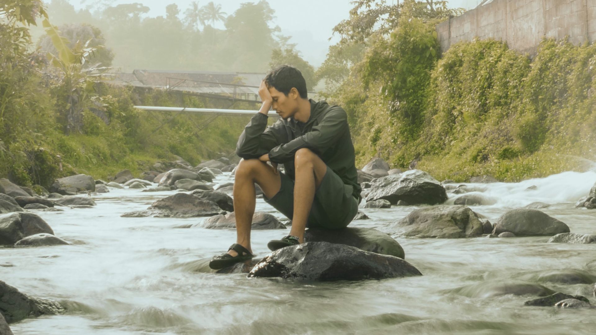a man sitting on a rock next to a river