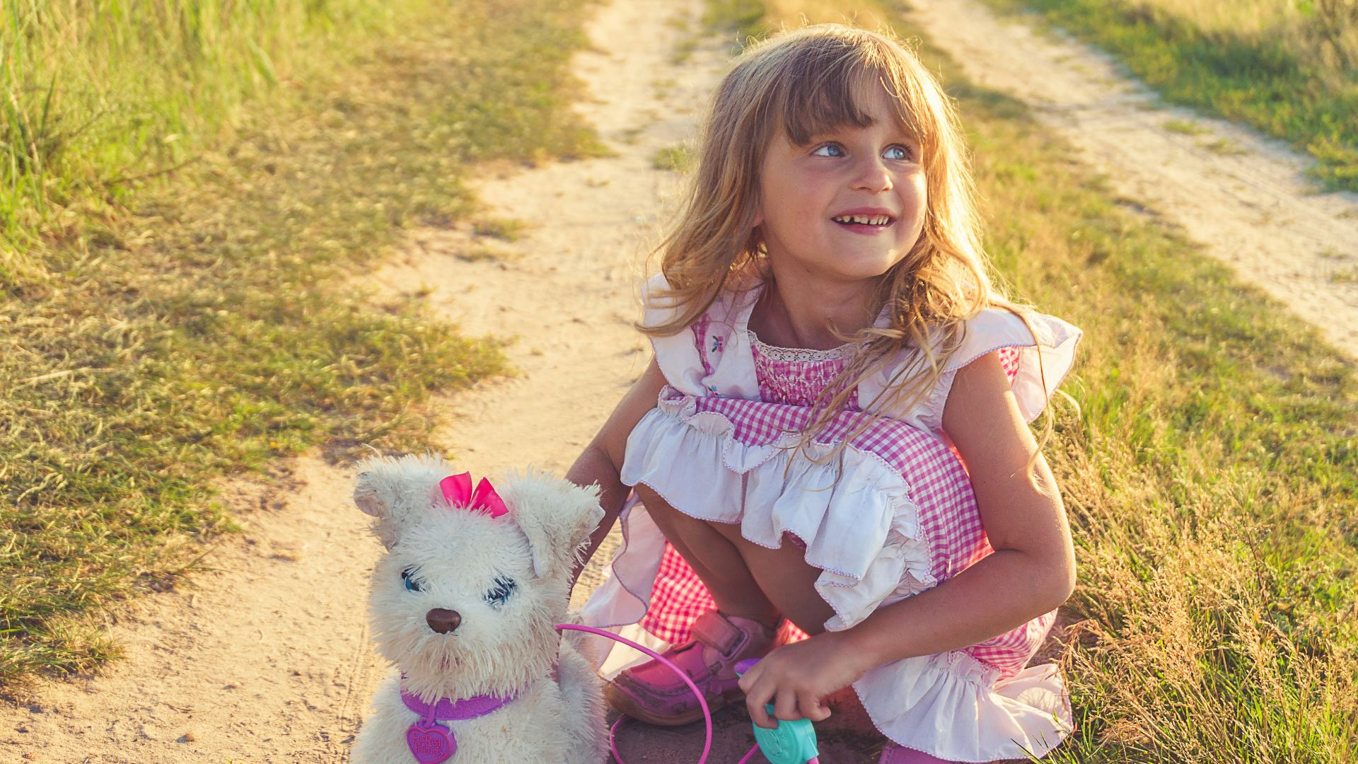 girl in pink and white dress holding white dog plush toy