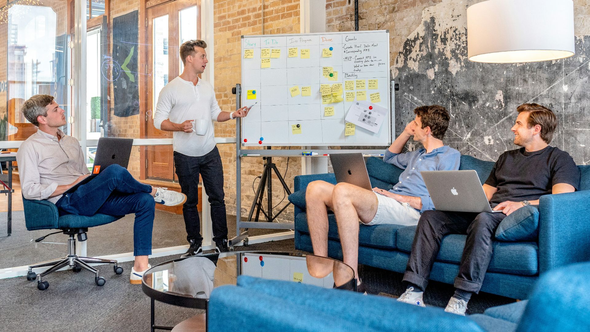 three men sitting while using laptops and watching man beside whiteboard