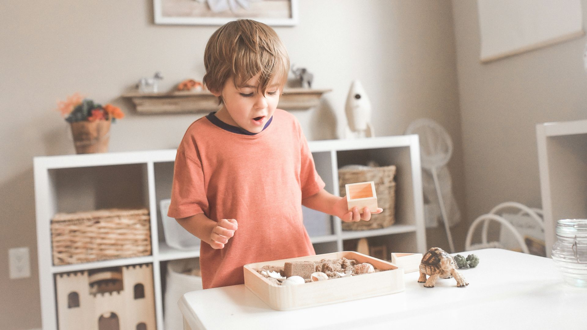 boy in orange crew neck t-shirt standing in front of white wooden table with cupcakes