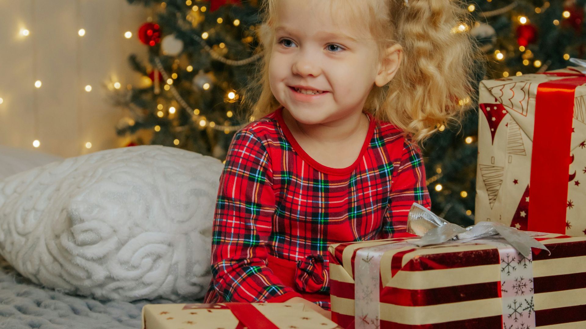 a little girl sitting on a bed next to presents