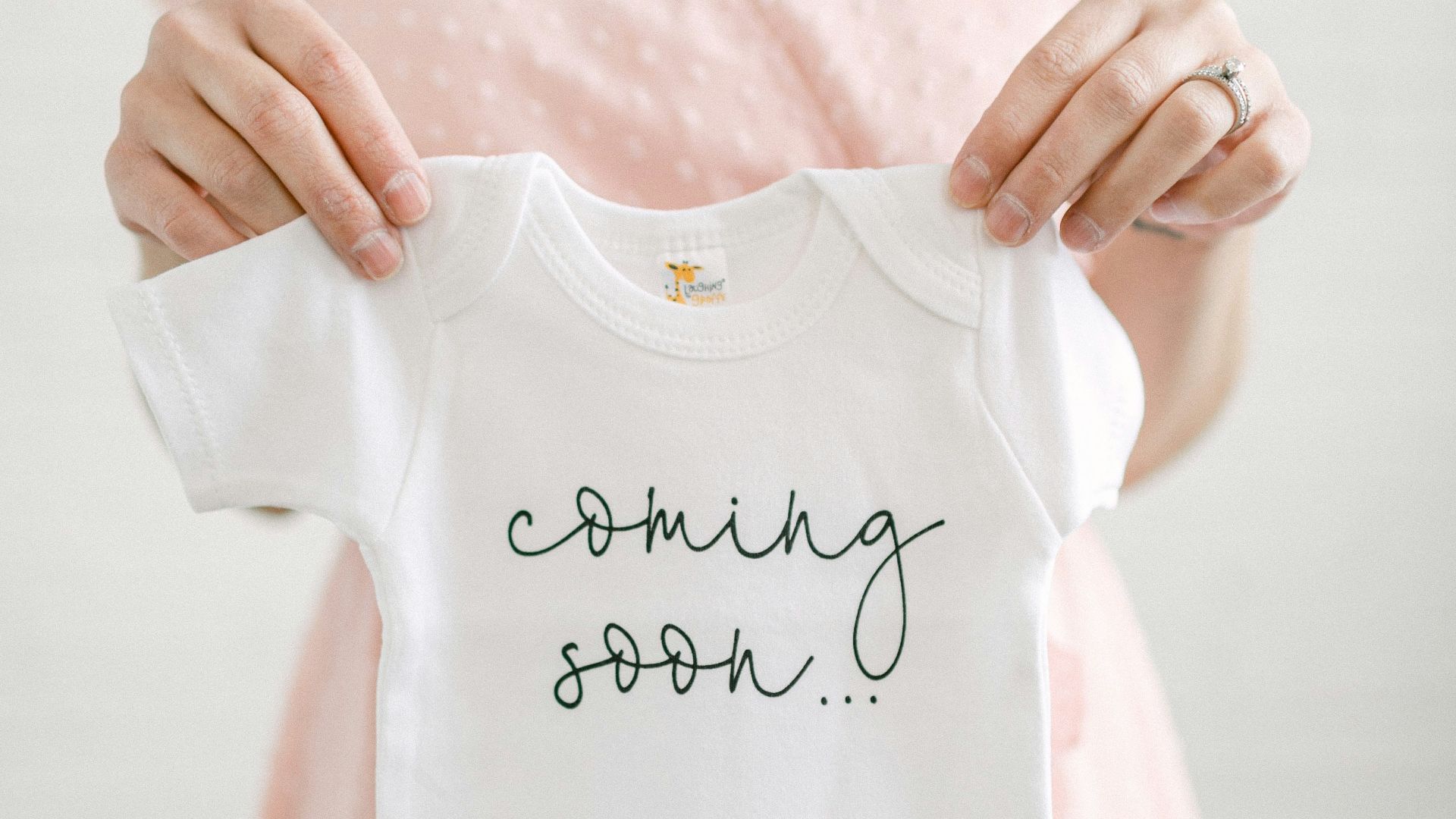 a woman holding a baby's shirt that says coming soon