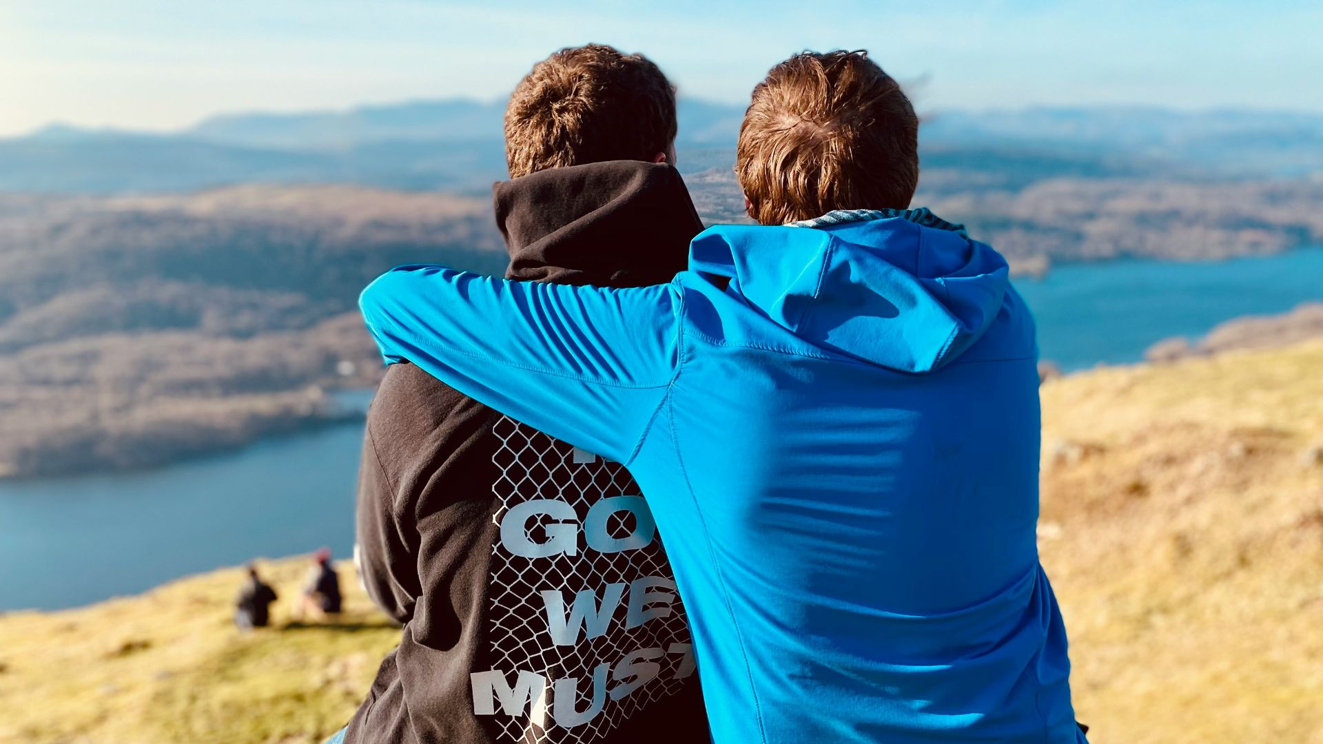 two people sitting on a hill overlooking a lake