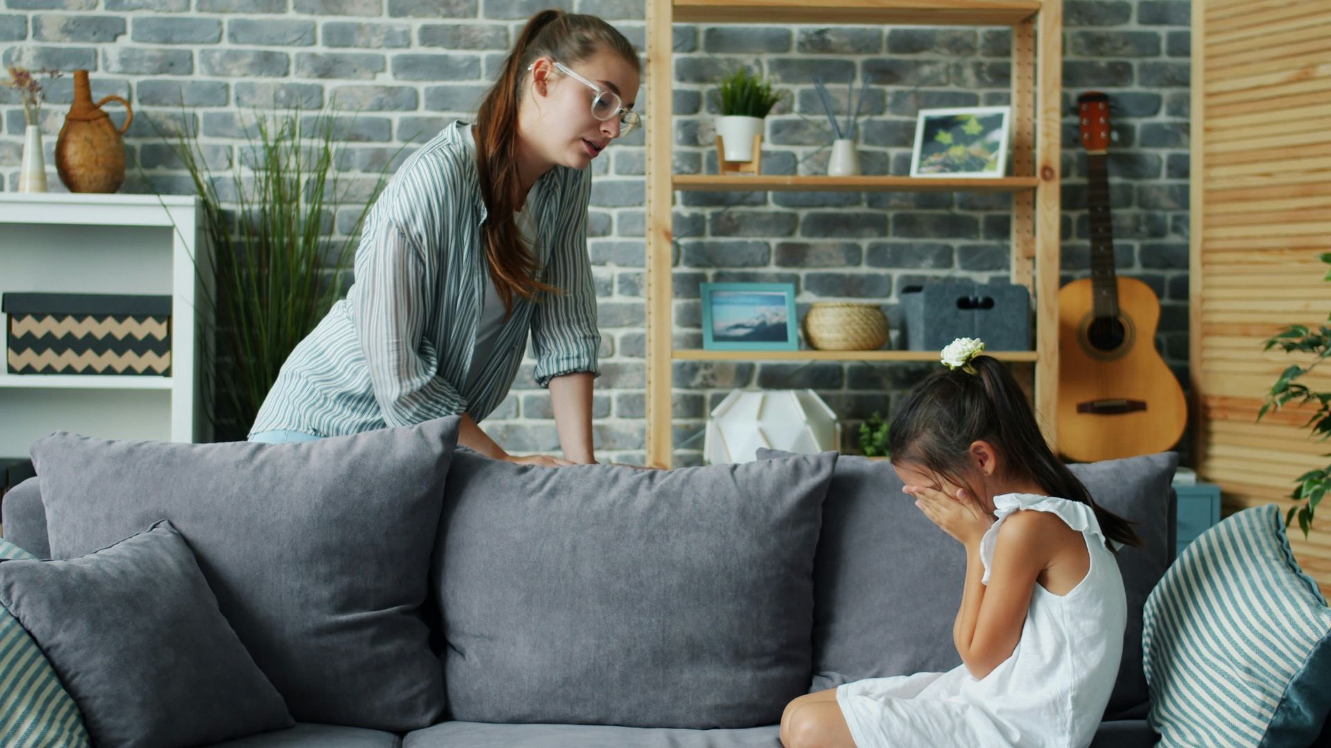 Mother scolds crying daughter on sofa in living room.