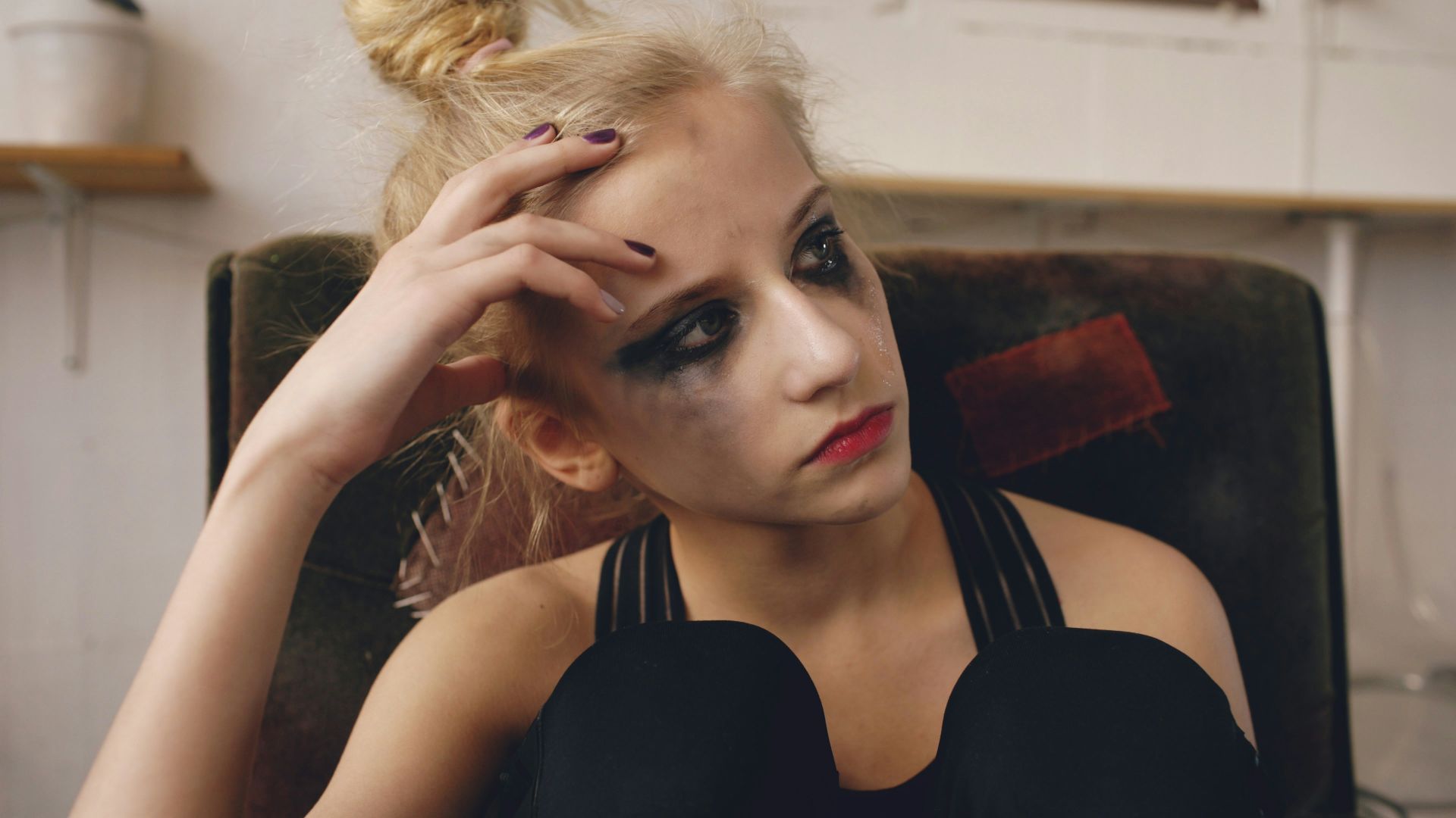 Young woman with smudged makeup sits in chair.
