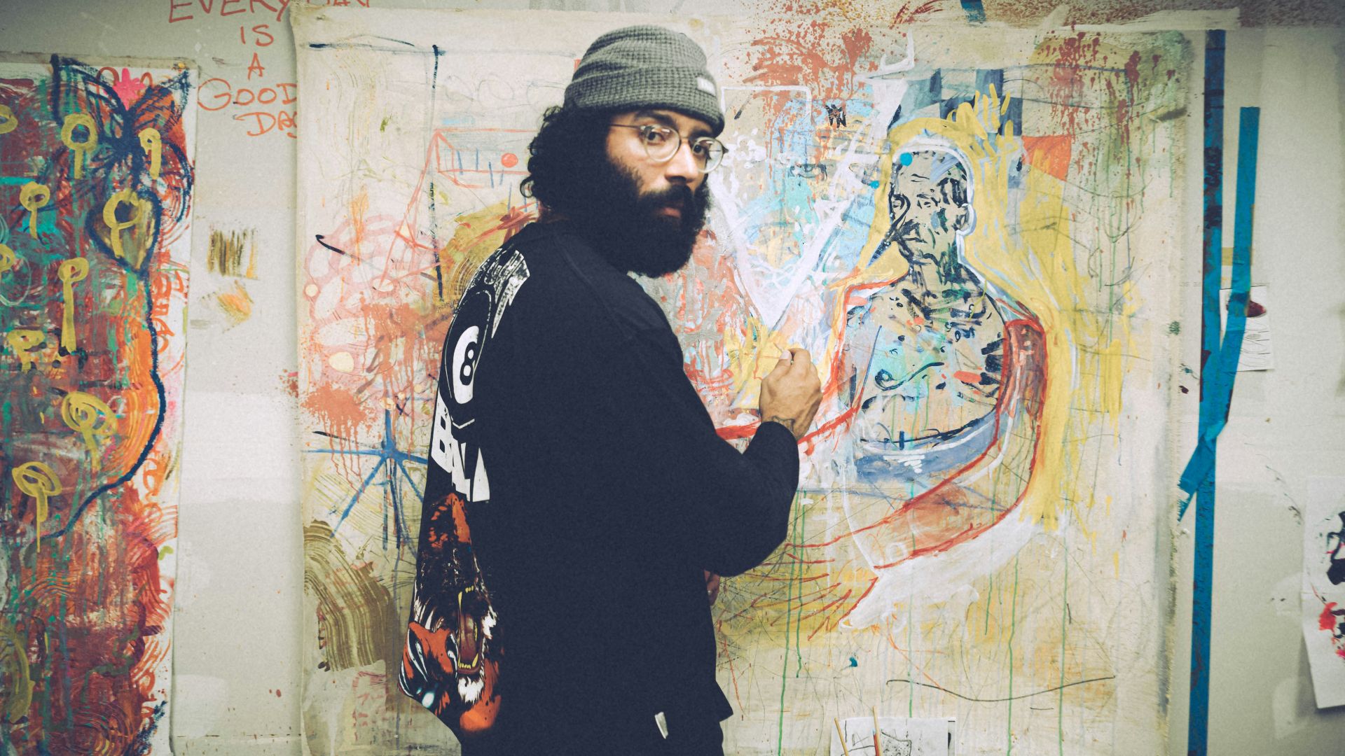 man in black and white sweater standing beside wall with graffiti