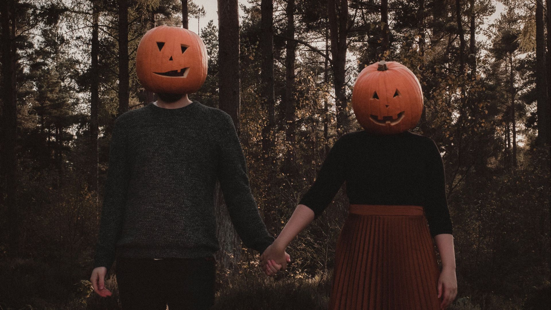 a man and a woman holding hands with pumpkins on their heads