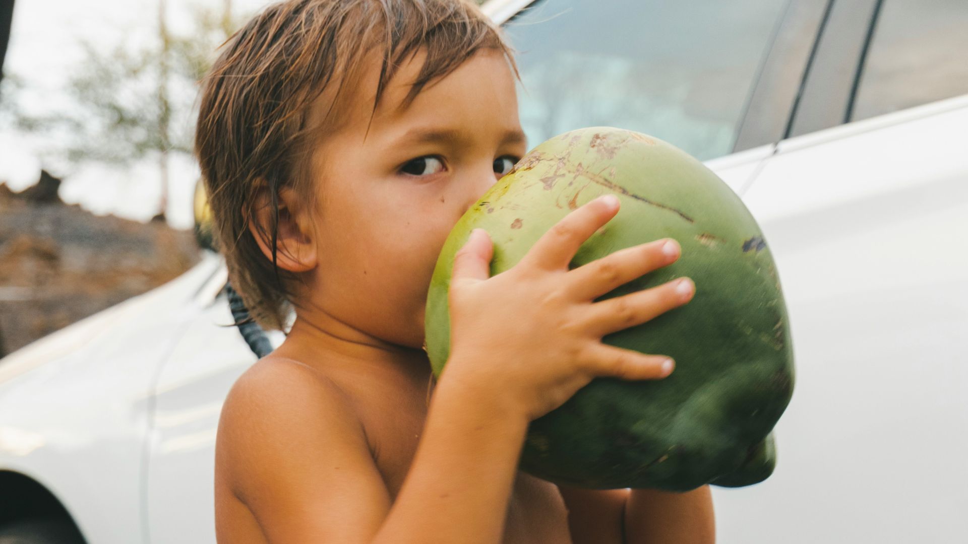 woman in blue and white polka dot tank top holding green watermelon